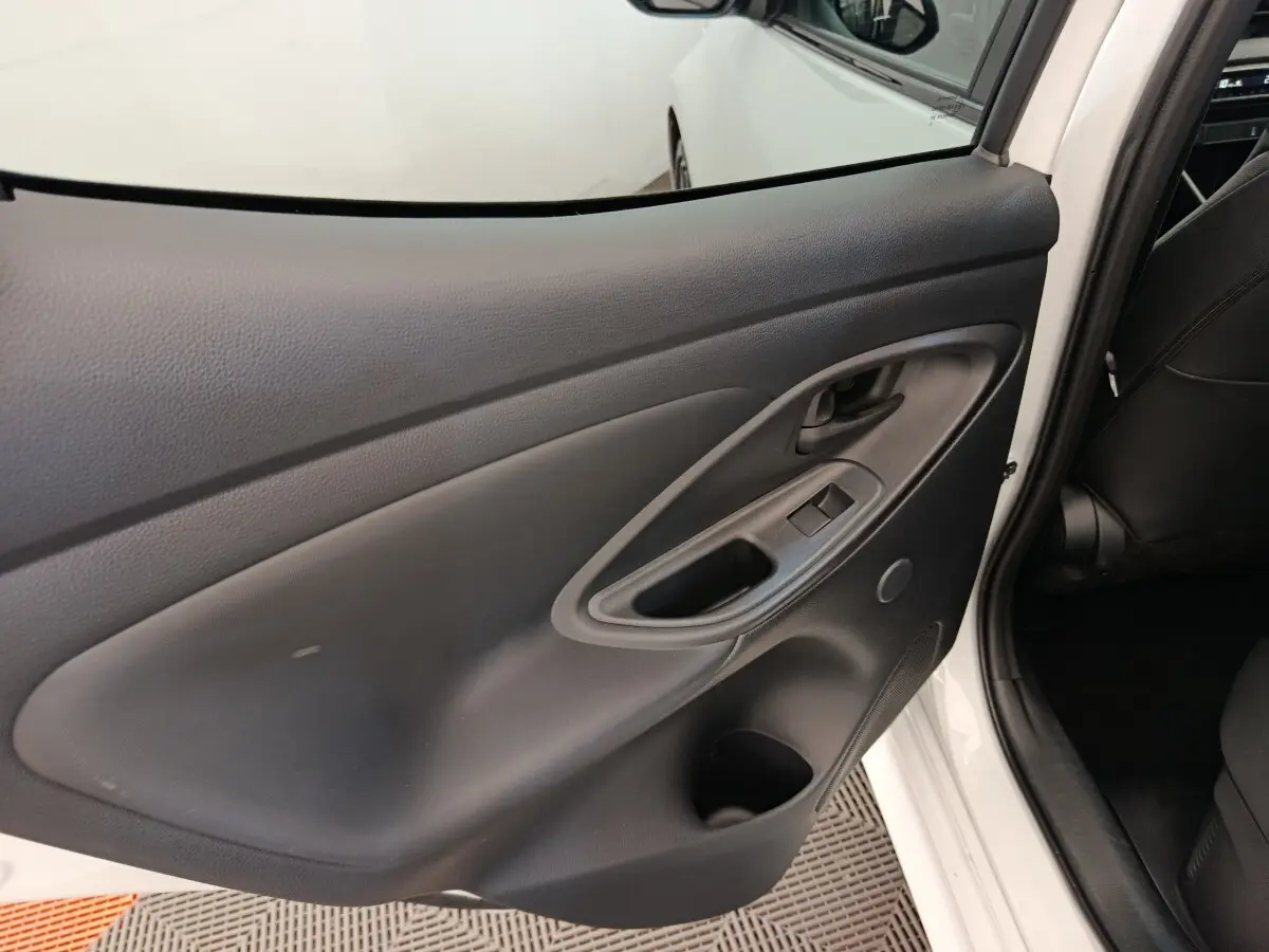 Vue intérieure de la porte arrière gauche noire d'une Toyota Yaris hybride blanche, avec poignée et commandes de fenêtre.