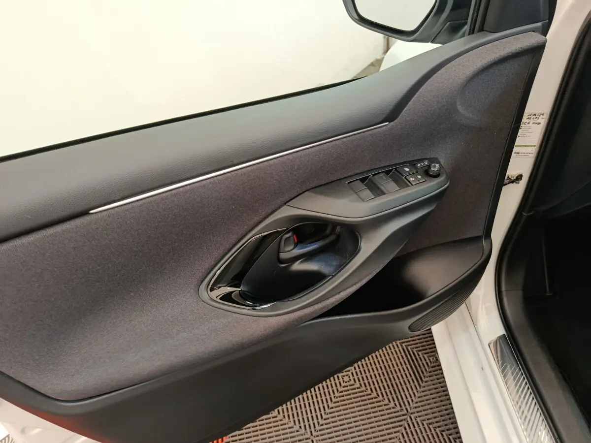 Vue intérieure côté conducteur de la porte d'une Toyota Yaris Hybride blanche, avec commandes électriques et poignée noire.
