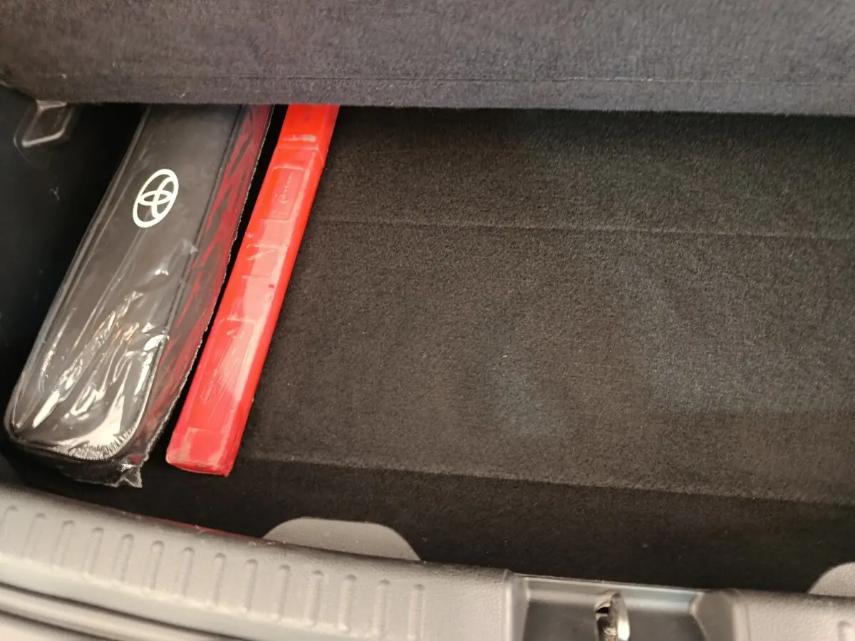 Coffre ouvert de Toyota Yaris Hybride blanc, vue plongeante sur tapis noir avec kit de sécurité rangé sur le côté.