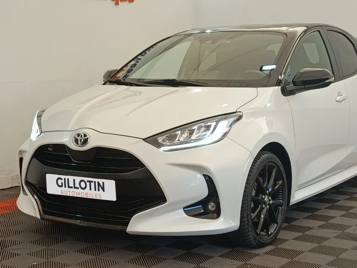 Toyota Yaris Hybride 116h blanc vue 3/4 avant droit avec calandre noire et jantes alliage noires.