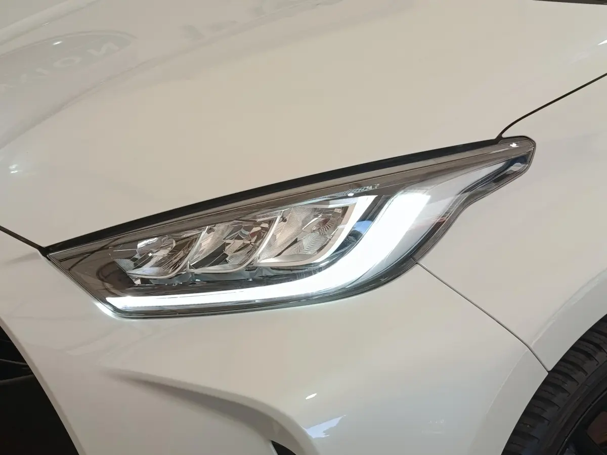 Gros plan sur le phare avant droit LED d'une Toyota Yaris Hybride blanche, soulignant ses lignes modernes et précises.
