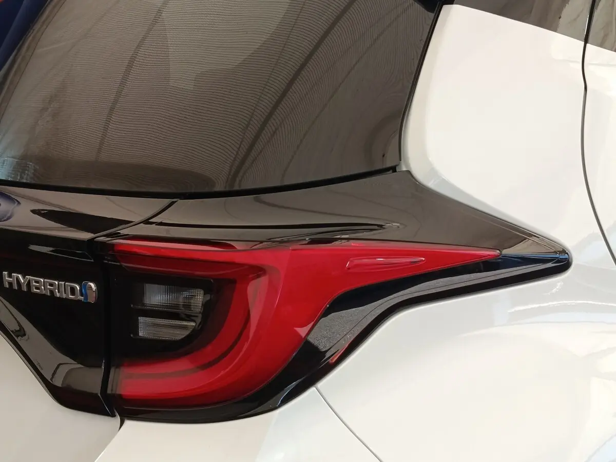 Gros plan sur le feu arrière droit rouge et noir d’une Toyota Yaris Hybride blanche, avec logo Hybrid visible.