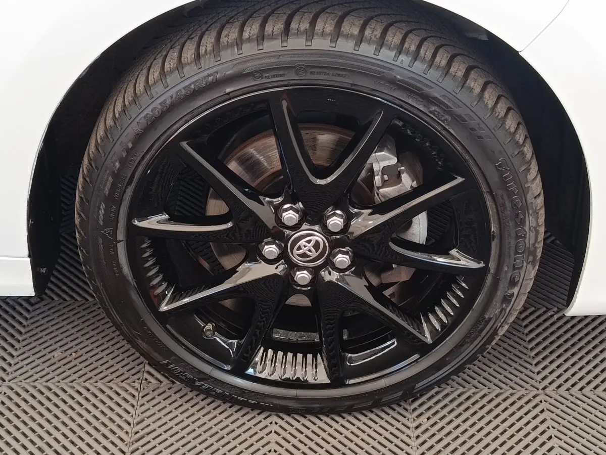 Gros plan sur la roue avant droite noire brillante d'une Toyota Yaris hybride blanche, avec logo Toyota au centre.