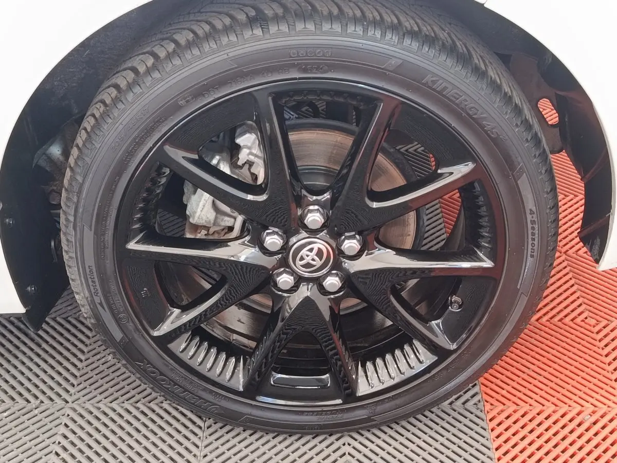 Gros plan sur la roue avant droite noire brillante d'une Toyota Yaris blanche hybride, avec logo Toyota au centre.