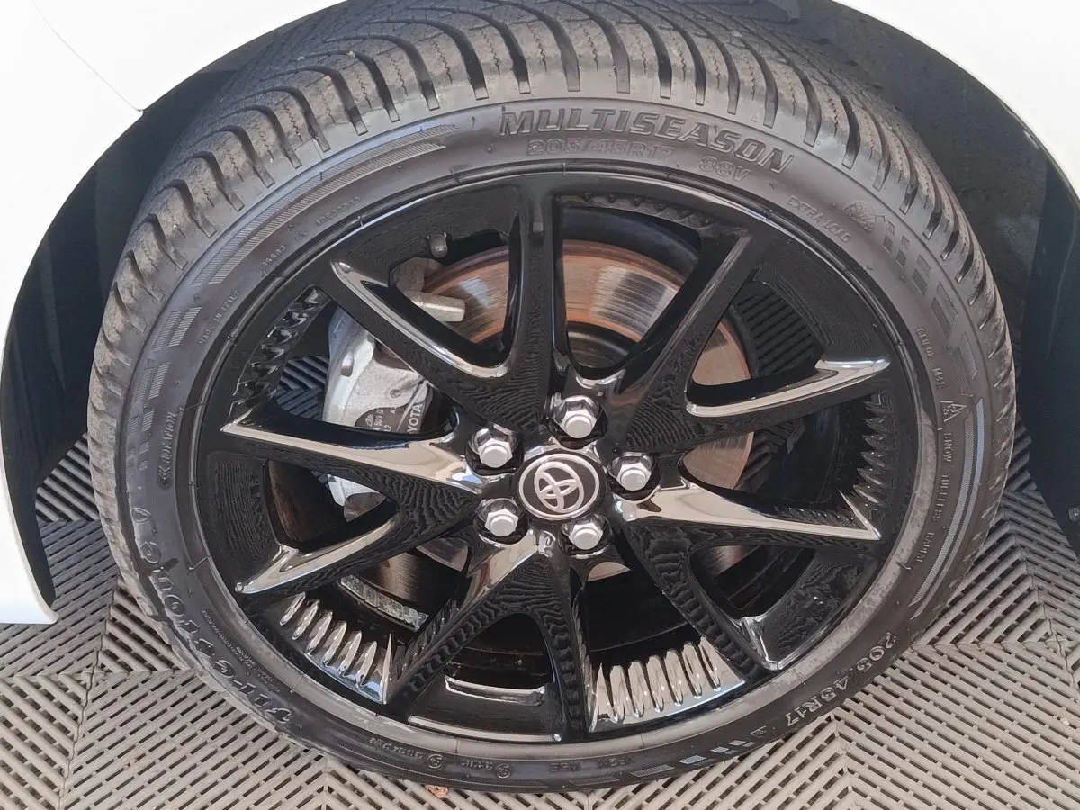 Gros plan sur la jante noire brillante et le pneu multisaison d’une Toyota Yaris blanche hybride 2022.