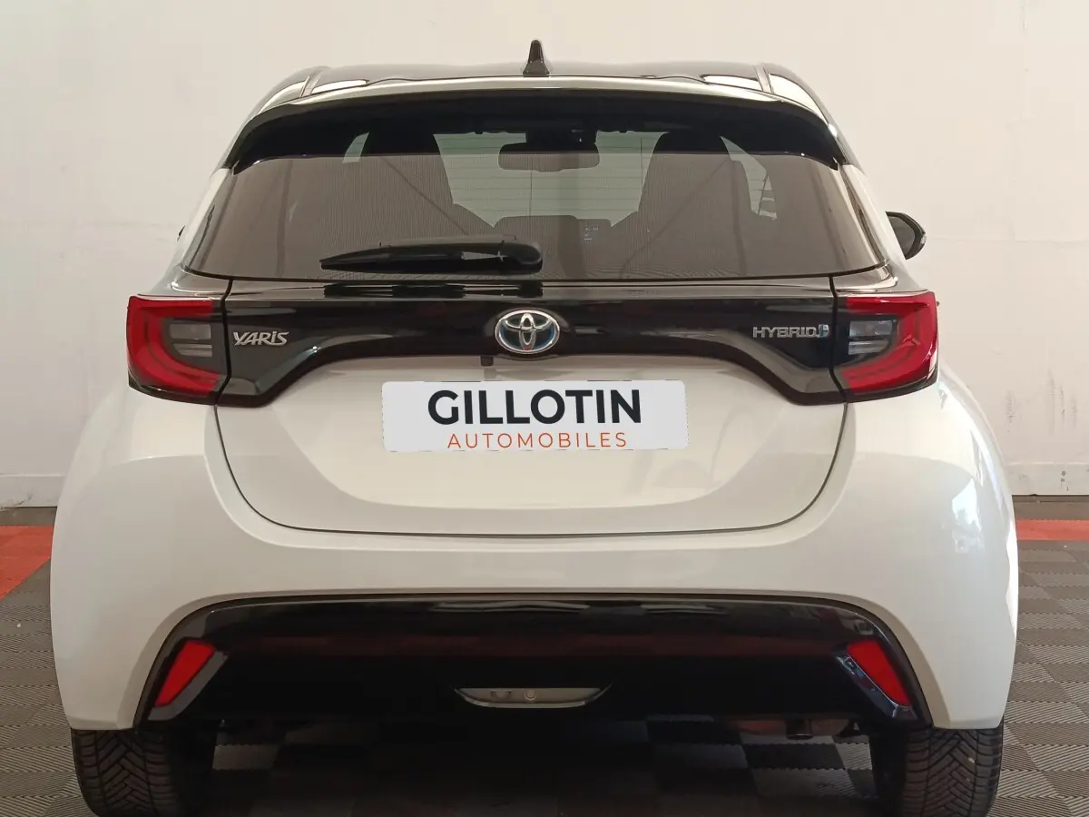 Vue arrière d'une Toyota Yaris Hybride blanche avec bandeau noir brillant et feux arrière rouges distinctifs.