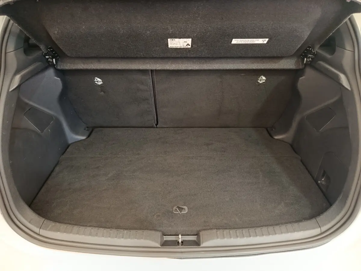 Coffre ouvert de la Toyota Yaris Hybride 116h Collection blanche, montrant l'espace de chargement vide et la banquette arrière rabattable.