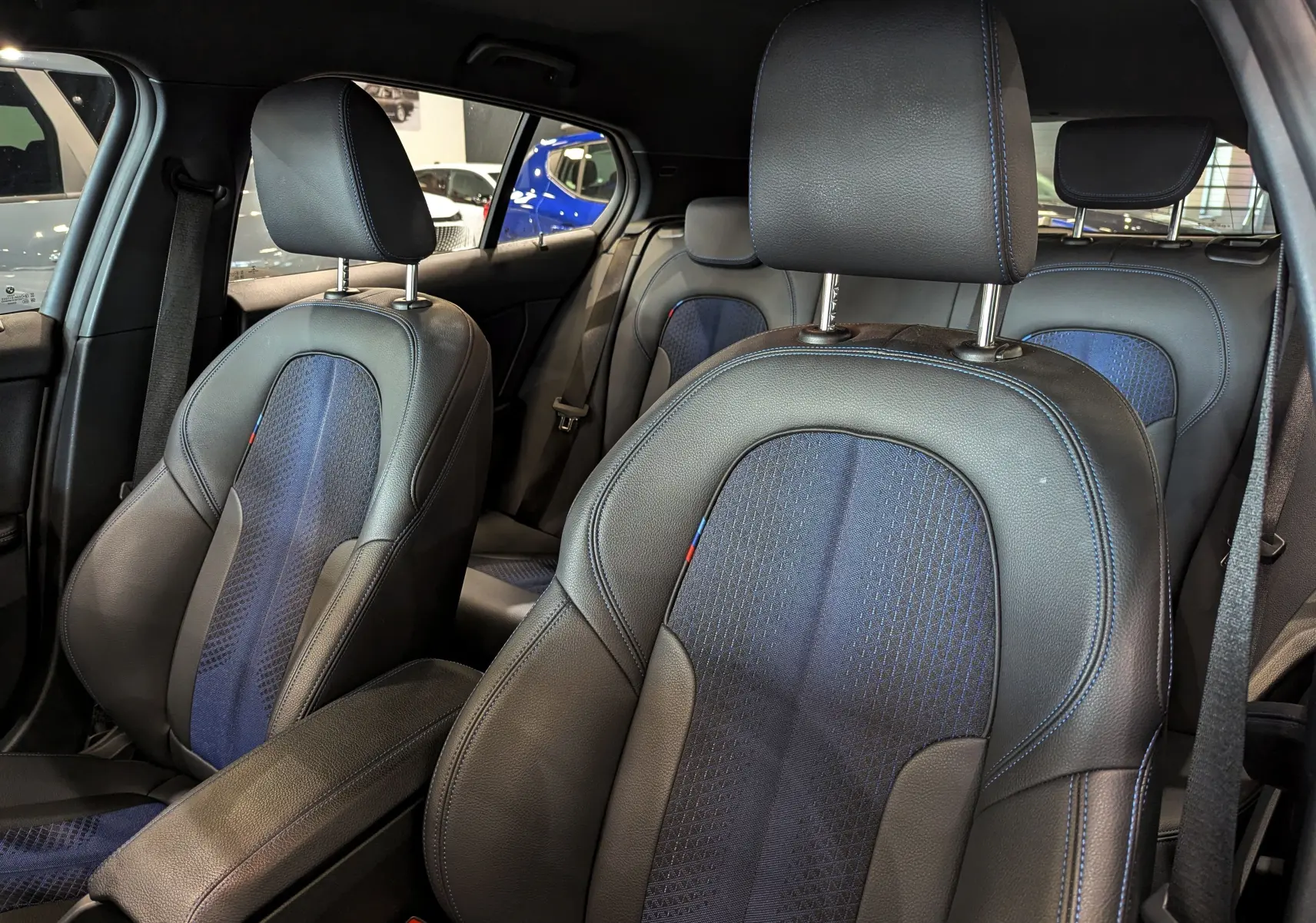 Vue intérieure sur les sièges avant en cuir noir et tissu bleu avec surpiqûres bleues de la BMW Série 1 F40 M Sport.