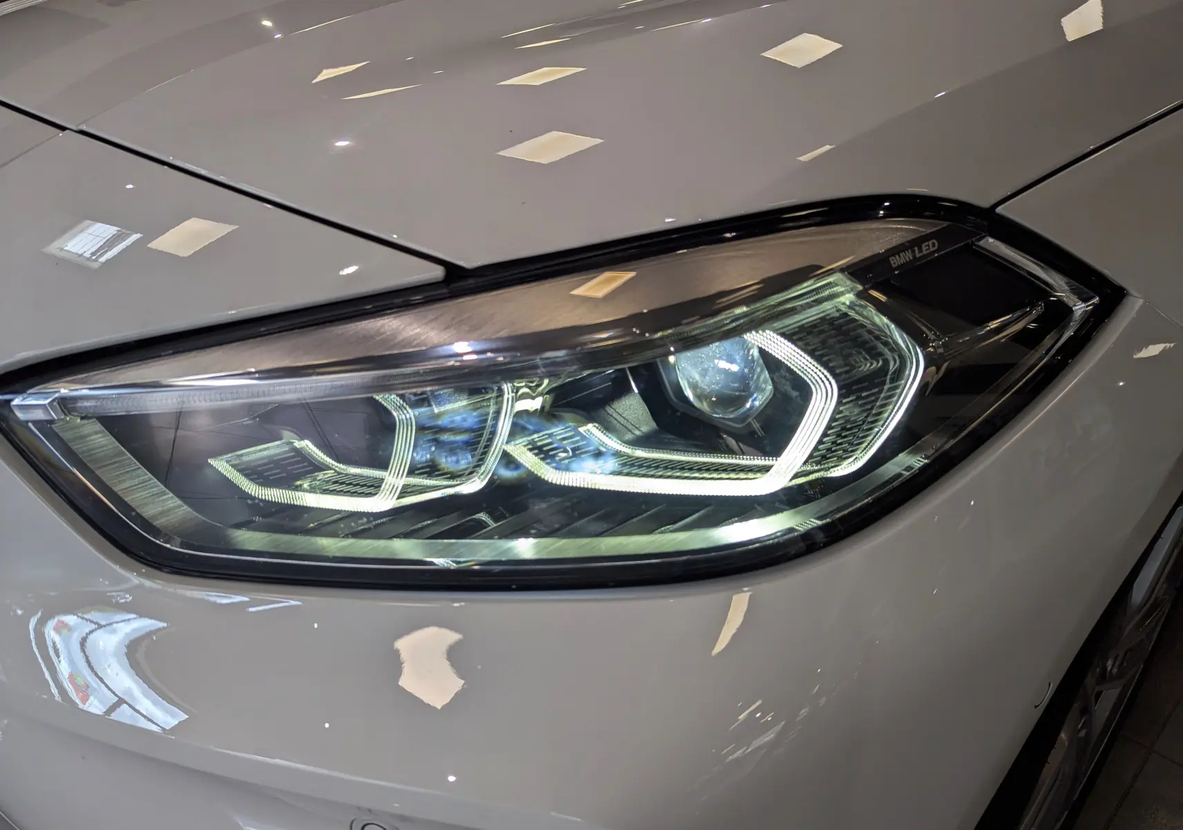 Gros plan sur le phare avant droit blanc alpin d'une BMW Série 1 F40 18d 2023 avec éclairage LED distinctif.