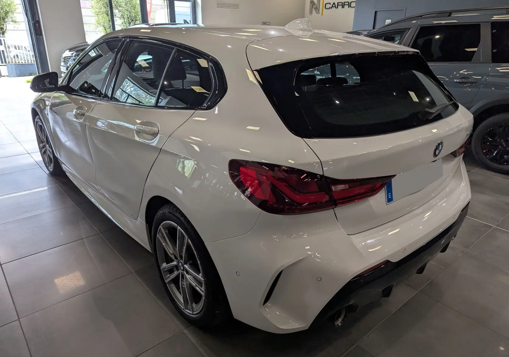 Vue 3/4 arrière droite d'une BMW Série 1 F40 blanche Alpine avec feux arrière LED et jantes alliage en showroom.