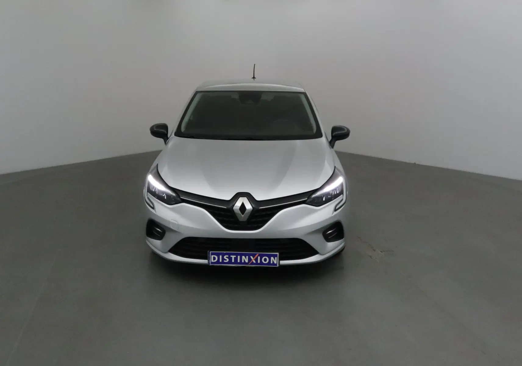 Renault Clio V gris platine vue de face avec phares LED allumés et calandre noire distinctive.