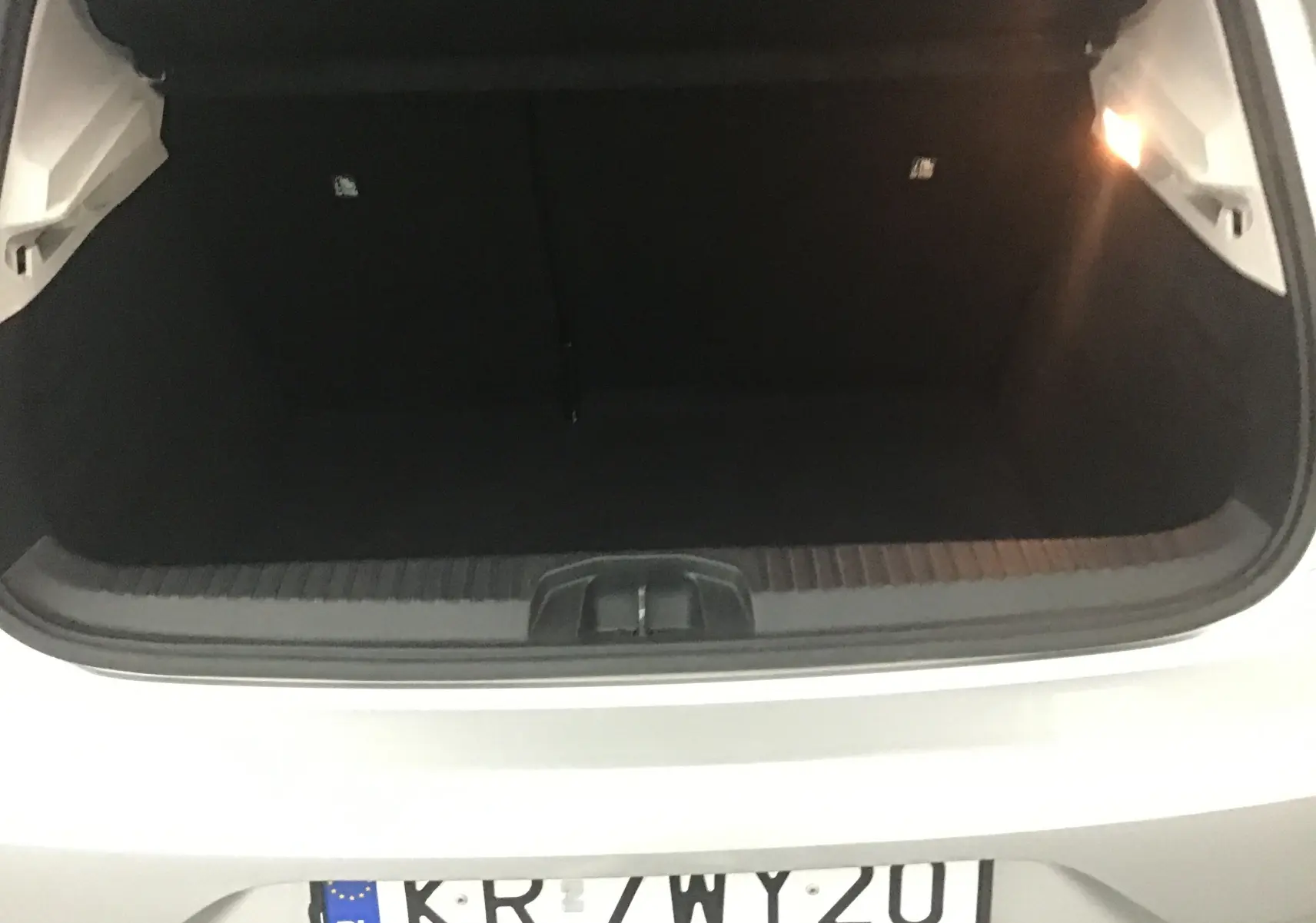 Coffre ouvert vu de l'arrière d'une Renault Clio V gris platine, montrant l'espace de chargement vide et l'éclairage intérieur.