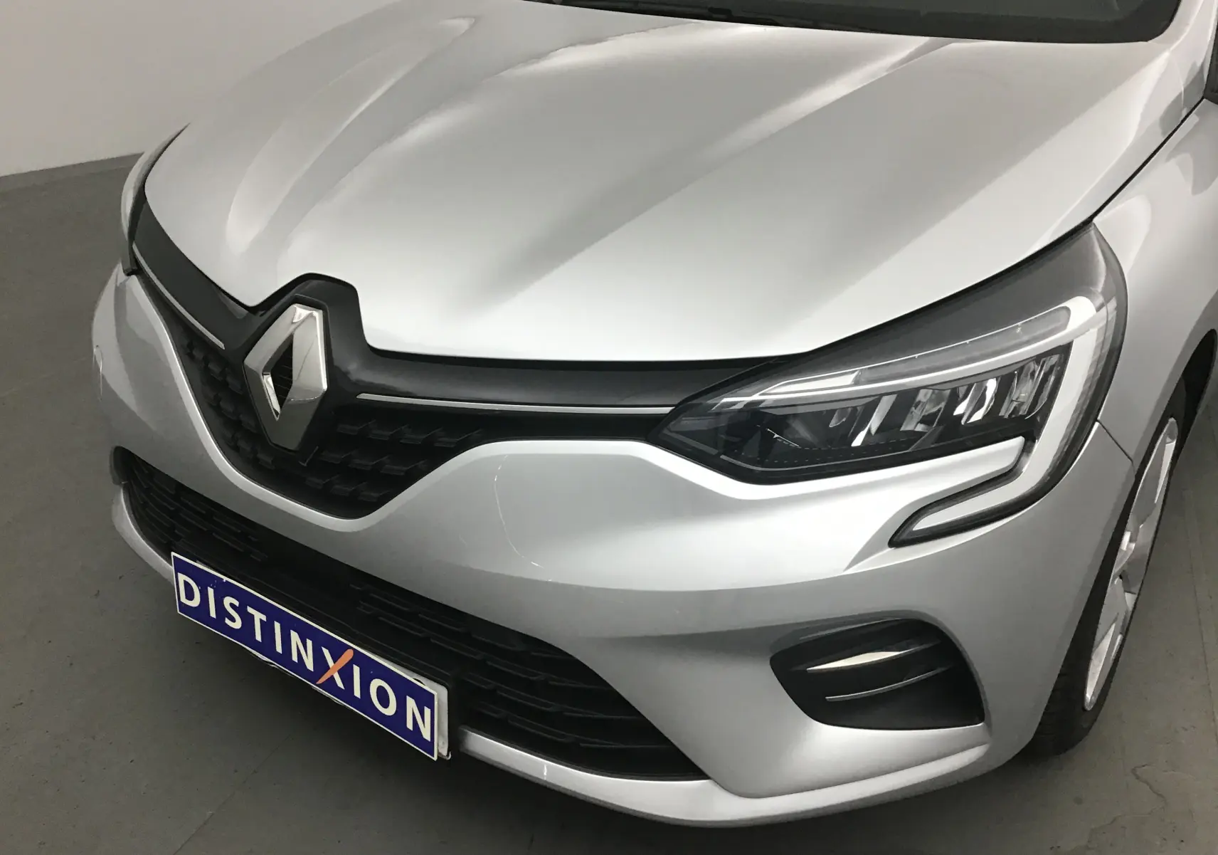 Vue 3/4 avant d'une Renault Clio V gris platine mettant en valeur ses phares LED et la calandre noire distinctive.