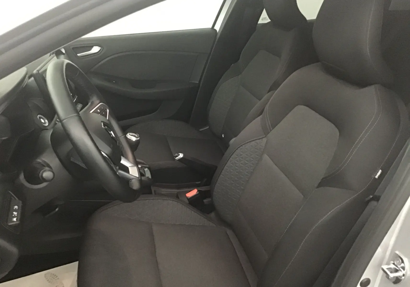 Vue intérieure côté conducteur de la Renault Clio V 1.0 TCE 90 Zen avec sièges tissu noir et volant multifonction.