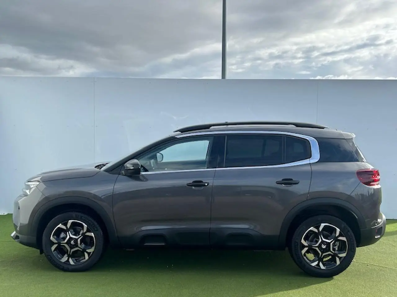Profil côté gauche d'un Citroën C5 Aircross gris platinium métallisé avec jantes alliage bi-ton et barres de toit noires.