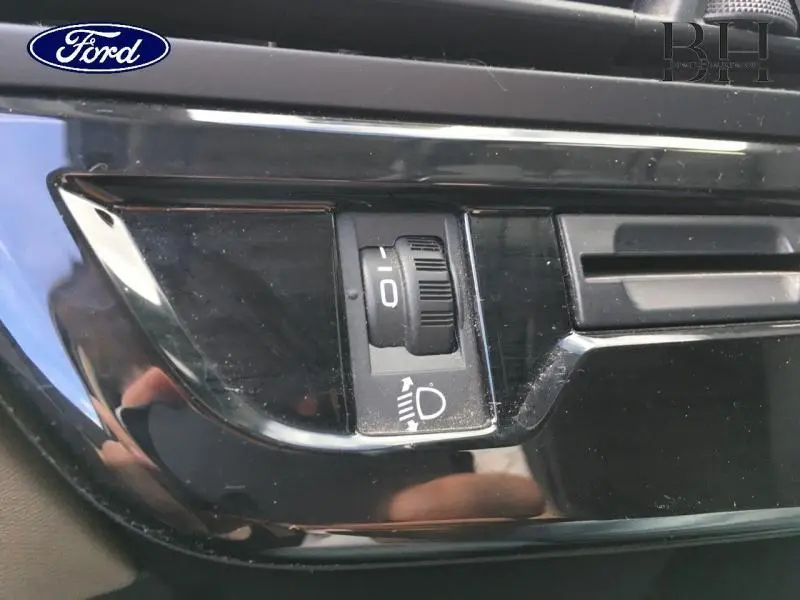 Gros plan sur le réglage de hauteur des phares dans l’habitacle noir brillant d’une Citroën C4 Picasso gris Shark.