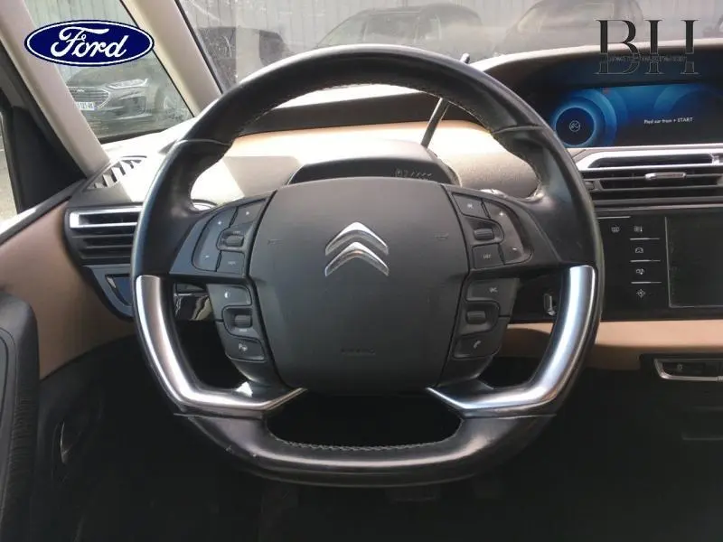 Vue rapprochée du volant cuir noir de la Citroën C4 Picasso 2016 avec commandes intégrées et tableau de bord beige.