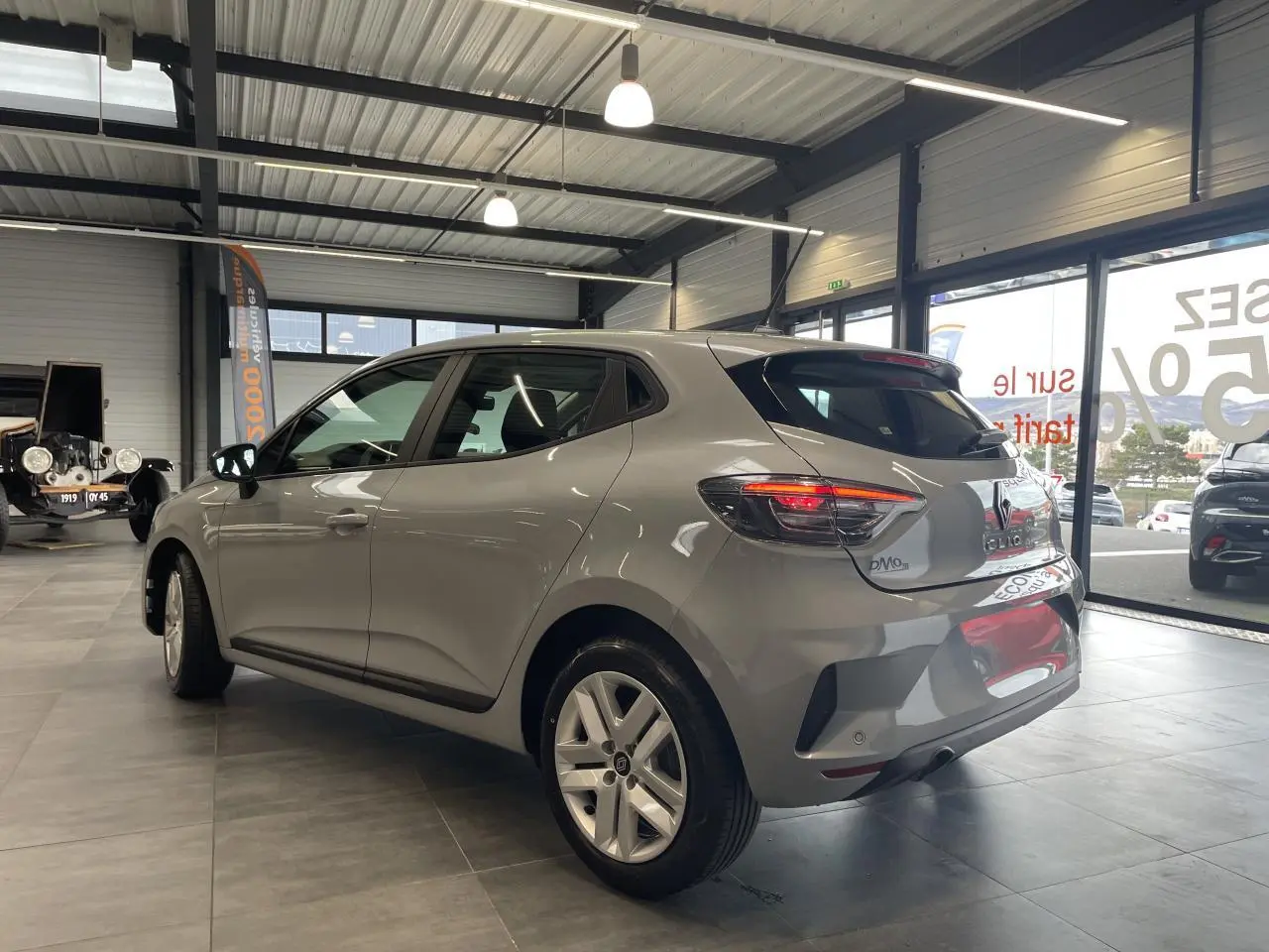 Renault Clio 2025 gris Rafale vue 3/4 arrière droit en intérieur, feux arrière LED allumés et jantes alliage.