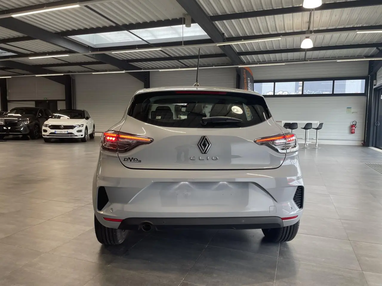 Vue arrière d'une Renault Clio 1.5 Blue dCi 2025 gris Rafale avec feux LED allumés dans un showroom.