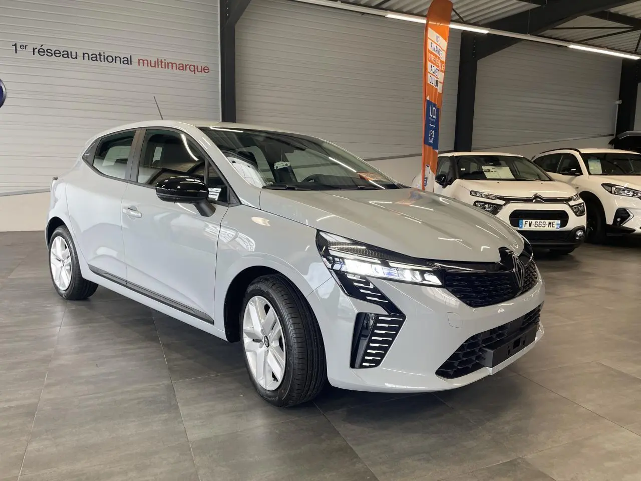 Renault Clio 2025 gris Rafale vue 3/4 avant droit en showroom avec détails noirs sur rétroviseurs et calandre.