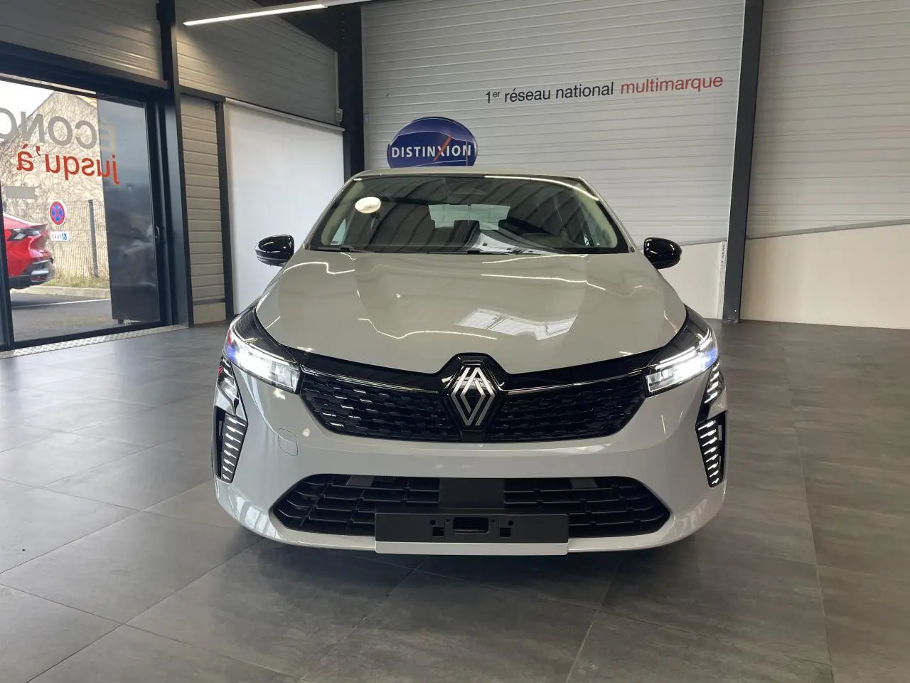 Vue de face d'une Renault Clio 1.5 Blue dCi 2025 gris Rafale avec calandre noire et feux LED allumés.