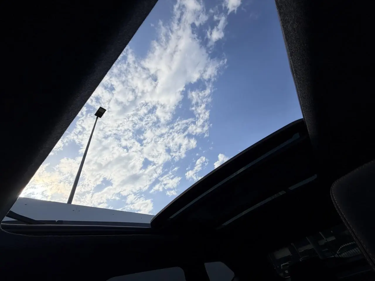 Vue intérieure du toit ouvrant panoramique du Dacia Bigster noir, avec ciel bleu et nuages visibles à travers le verre.