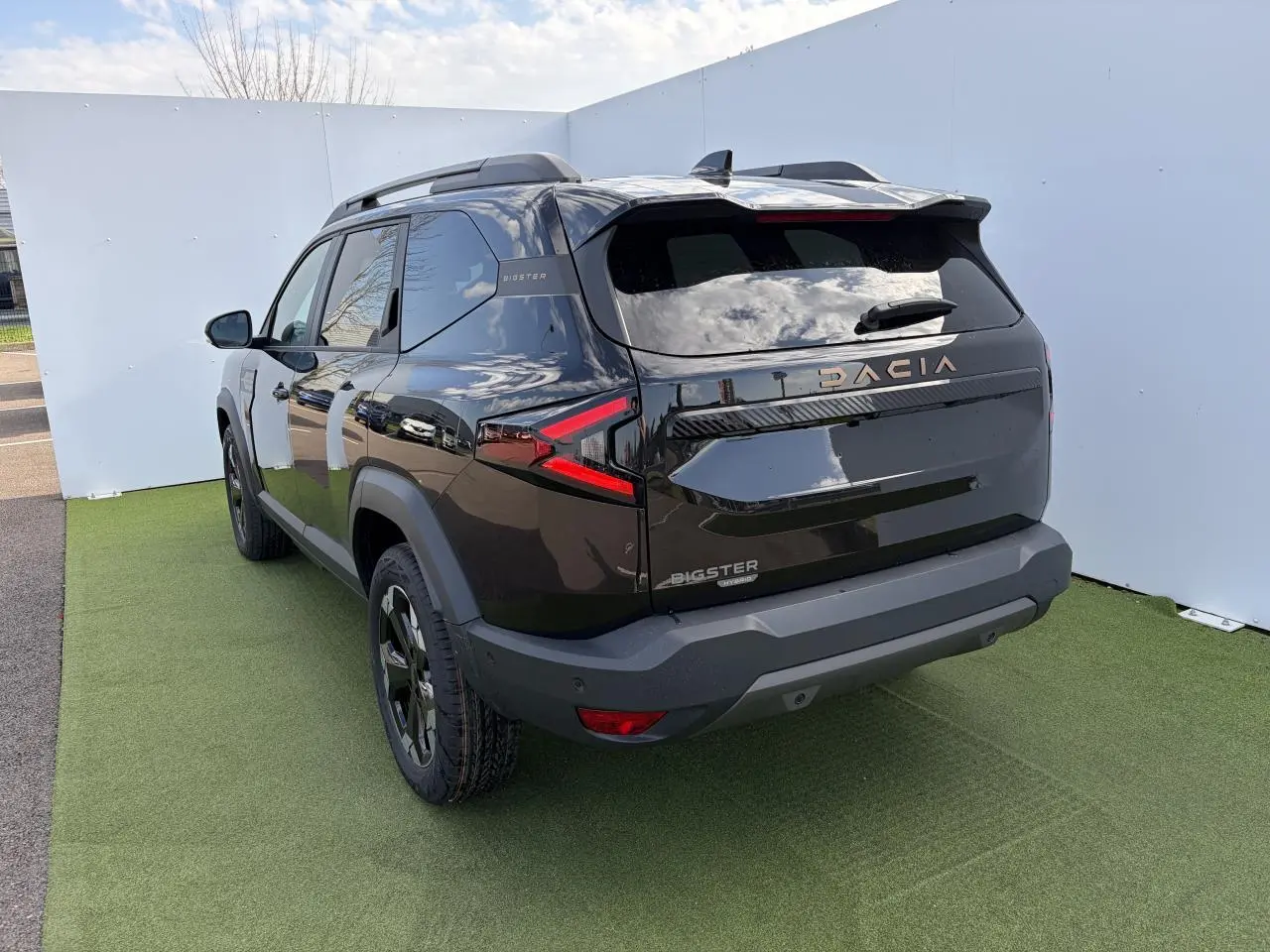 Vue 3/4 arrière droite du Dacia Bigster noir nacré avec signature lumineuse LED et barres de toit noires.