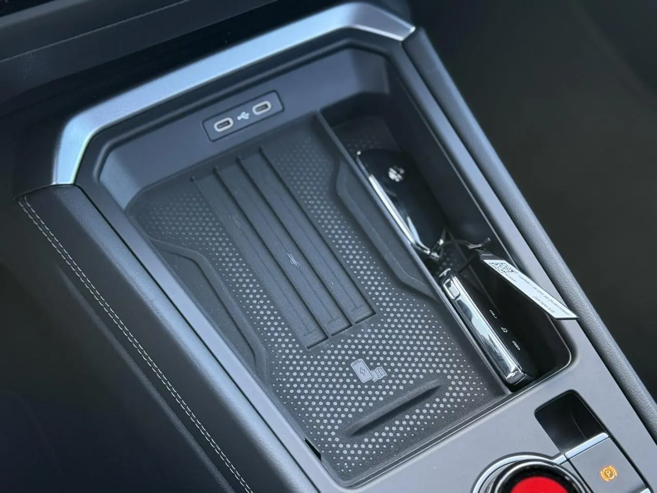 Vue rapprochée de la console centrale noire du Volkswagen T-Roc 2026 avec zone de charge sans fil et ports USB-C.