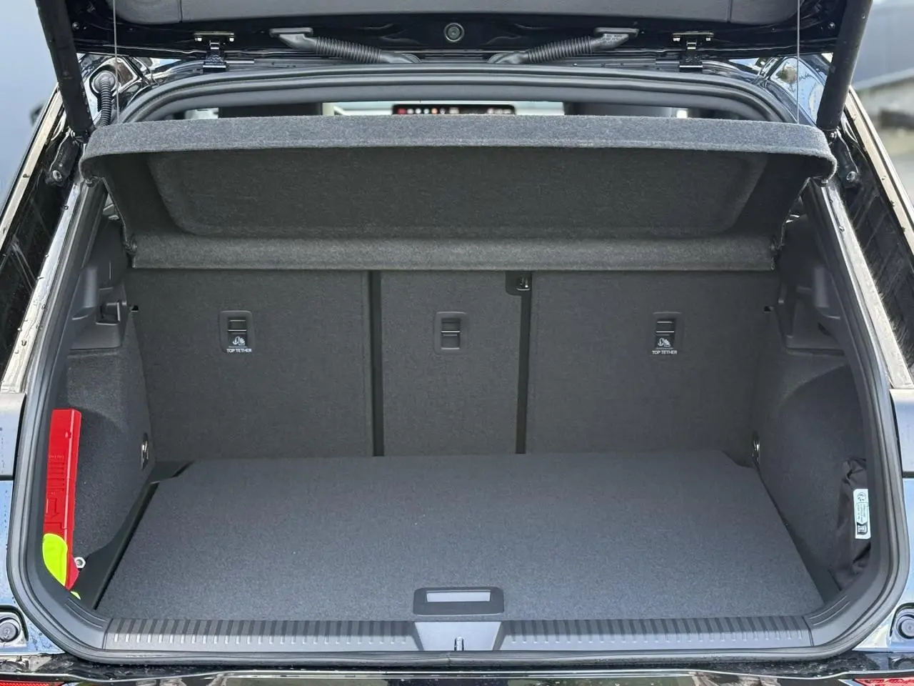 Coffre ouvert en vue arrière d’un Volkswagen T-Roc noir Ébène, montrant l’espace de chargement et la tablette de coffre relevée.