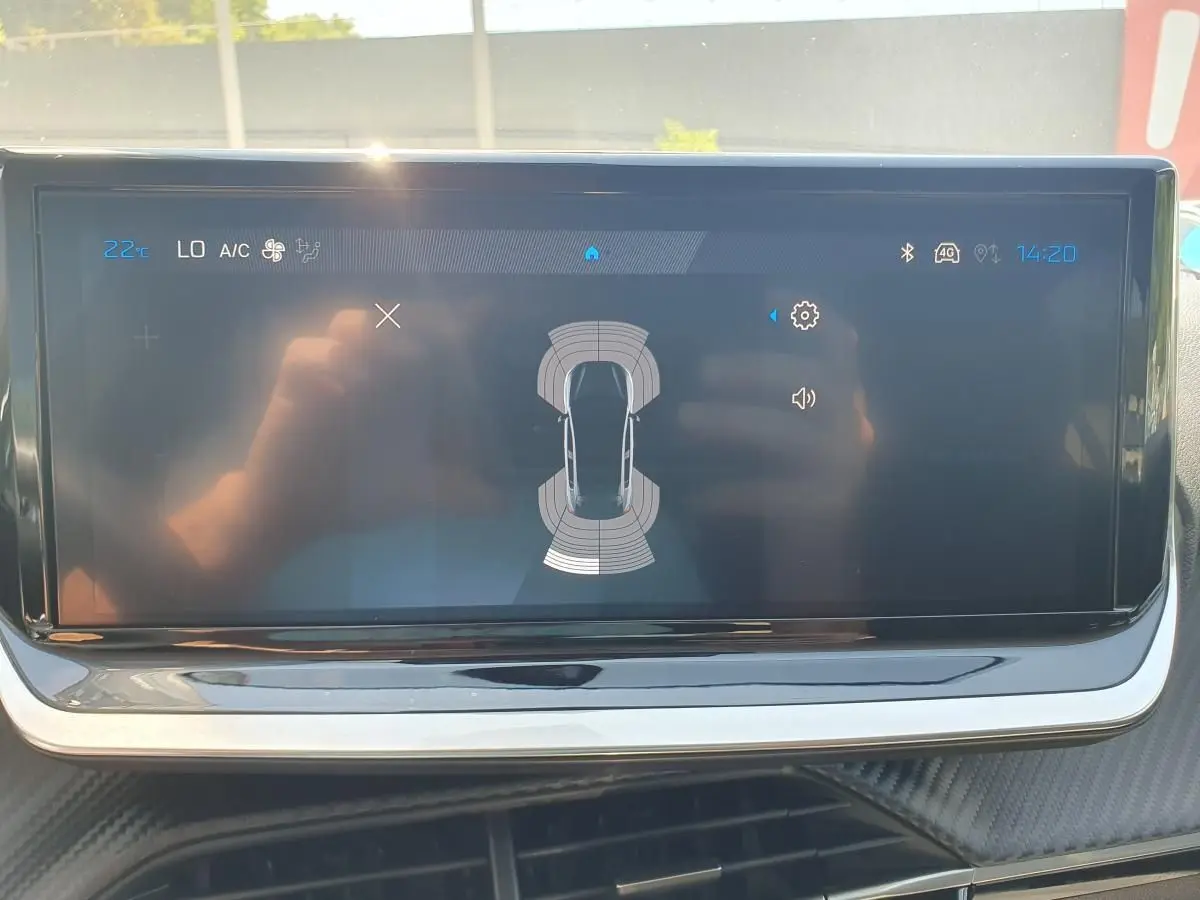 Écran tactile central de la Peugeot 208 1.2 Hybrid 110, affichant l'aide au stationnement avec vue de dessus du véhicule.