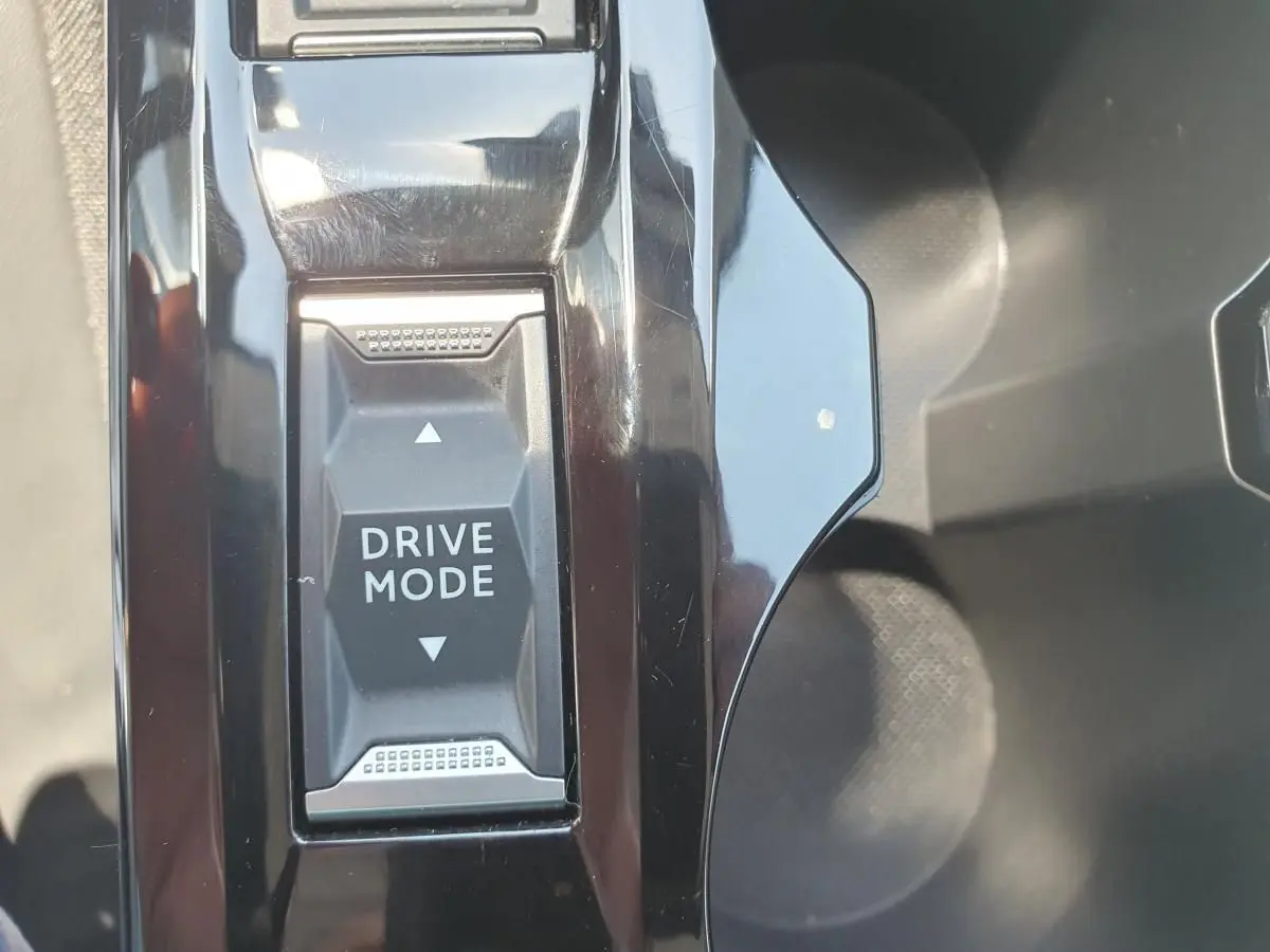 Gros plan sur le bouton Drive Mode au centre de la console noire brillante d'une Peugeot 208 gris Artense 2025.