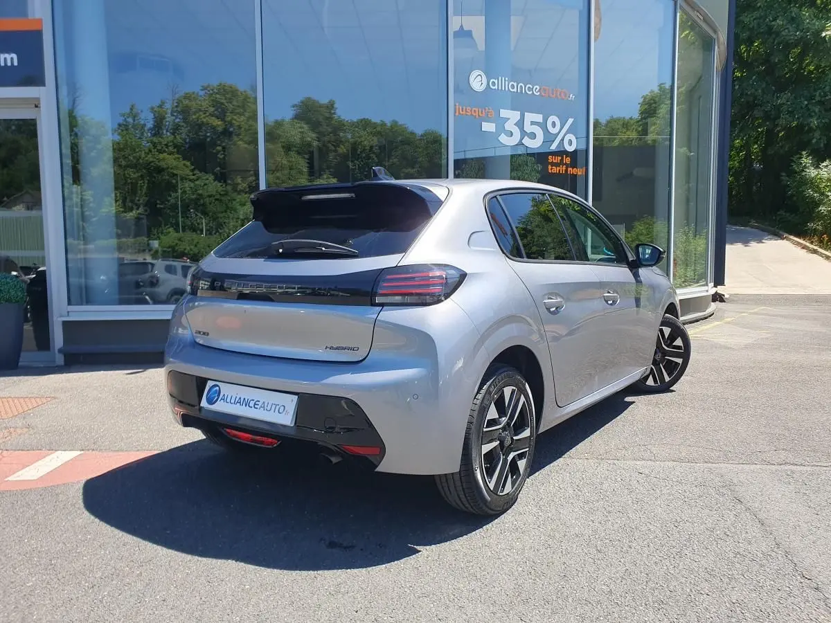 Vue 3/4 arrière droite d'une Peugeot 208 gris Artense avec jantes alliage bi-tons, garée devant un showroom.