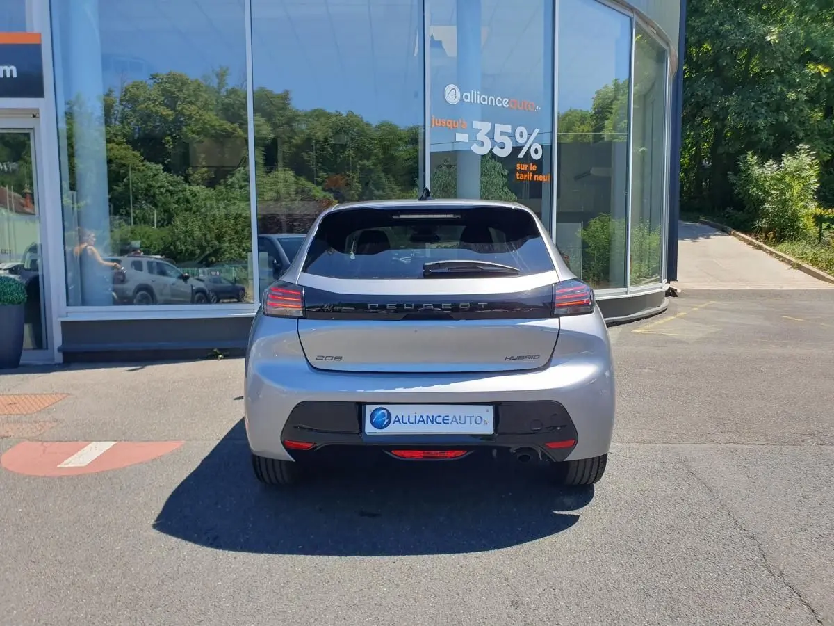 Vue arrière d'une Peugeot 208 hybride gris Artense stationnée devant une vitrine avec logo Alliance Auto.