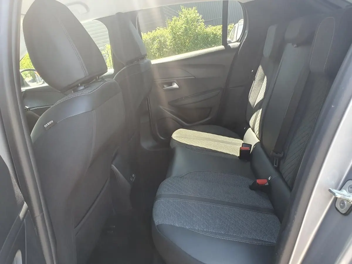 Vue intérieure côté arrière droit de la Peugeot 208 1.2 Hybrid 110 Allure, sièges tissu noir avec surpiqûres grises.