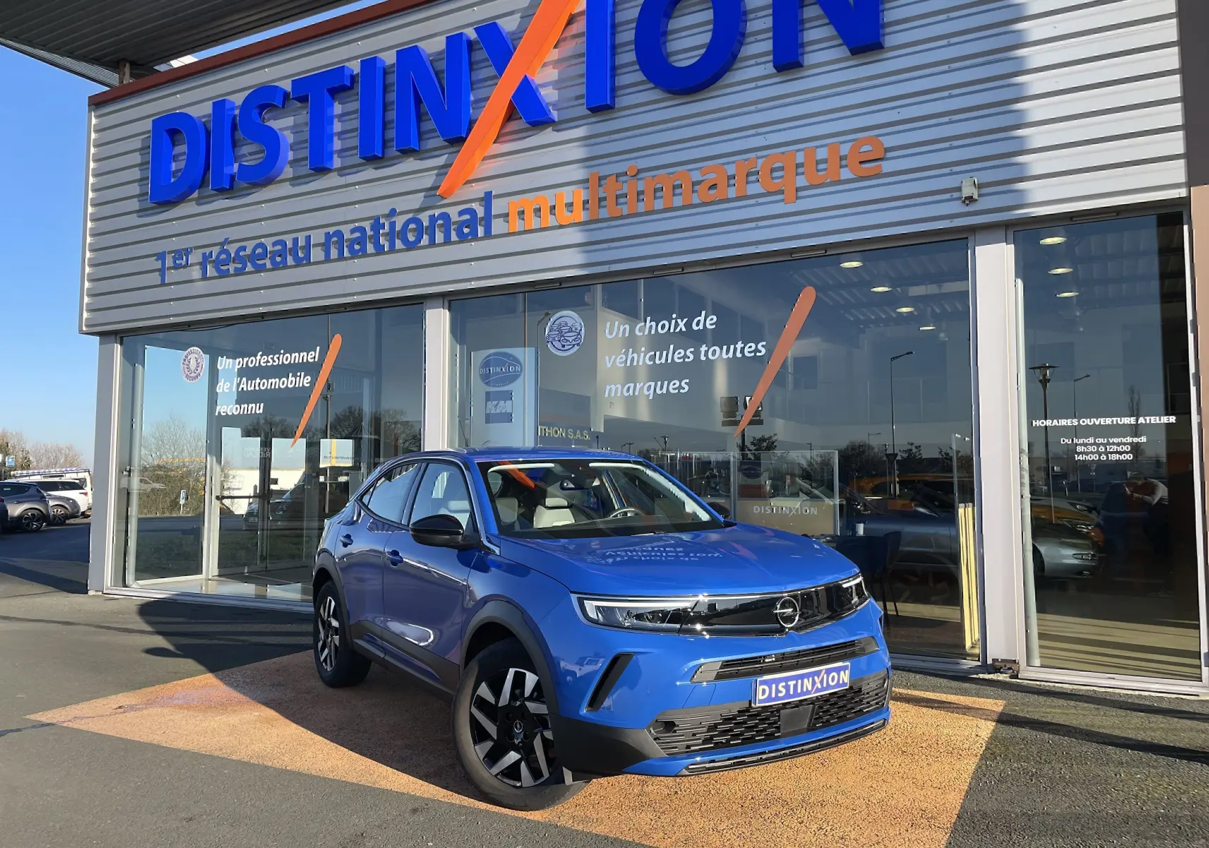 Opel Mokka bleu Voltak en 3/4 avant droit, stationné devant une concession Distinxion avec logo visible.