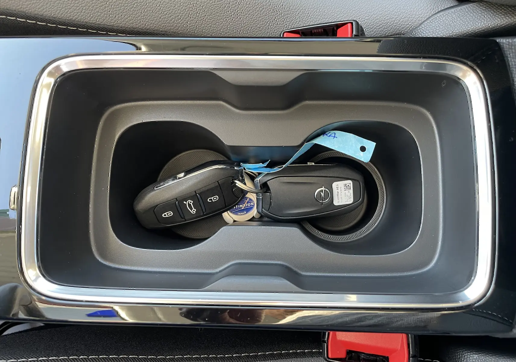 Gros plan sur la console centrale noire avec porte-clés Opel posé dans un compartiment rectangulaire.