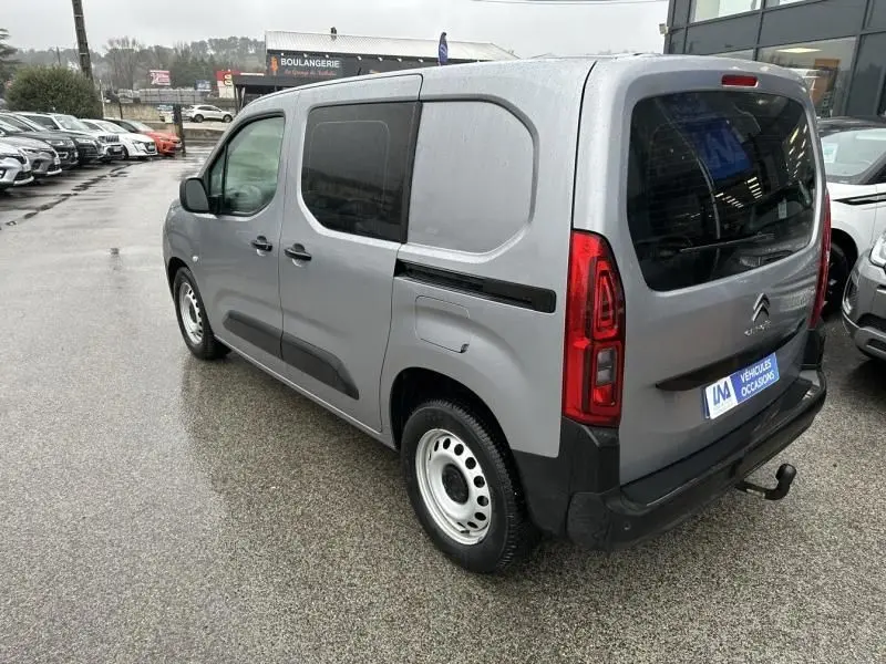 Vue 3/4 arrière droite d'un Citroën Berlingo van gris métal avec vitres arrière teintées et attelage visible.