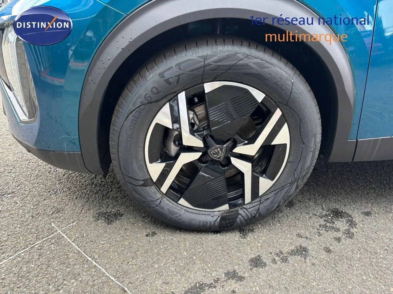 Gros plan sur la roue avant gauche du Peugeot 2008 Hybrid 136ch en bleu Obsession Metal avec jante noire et argentée.