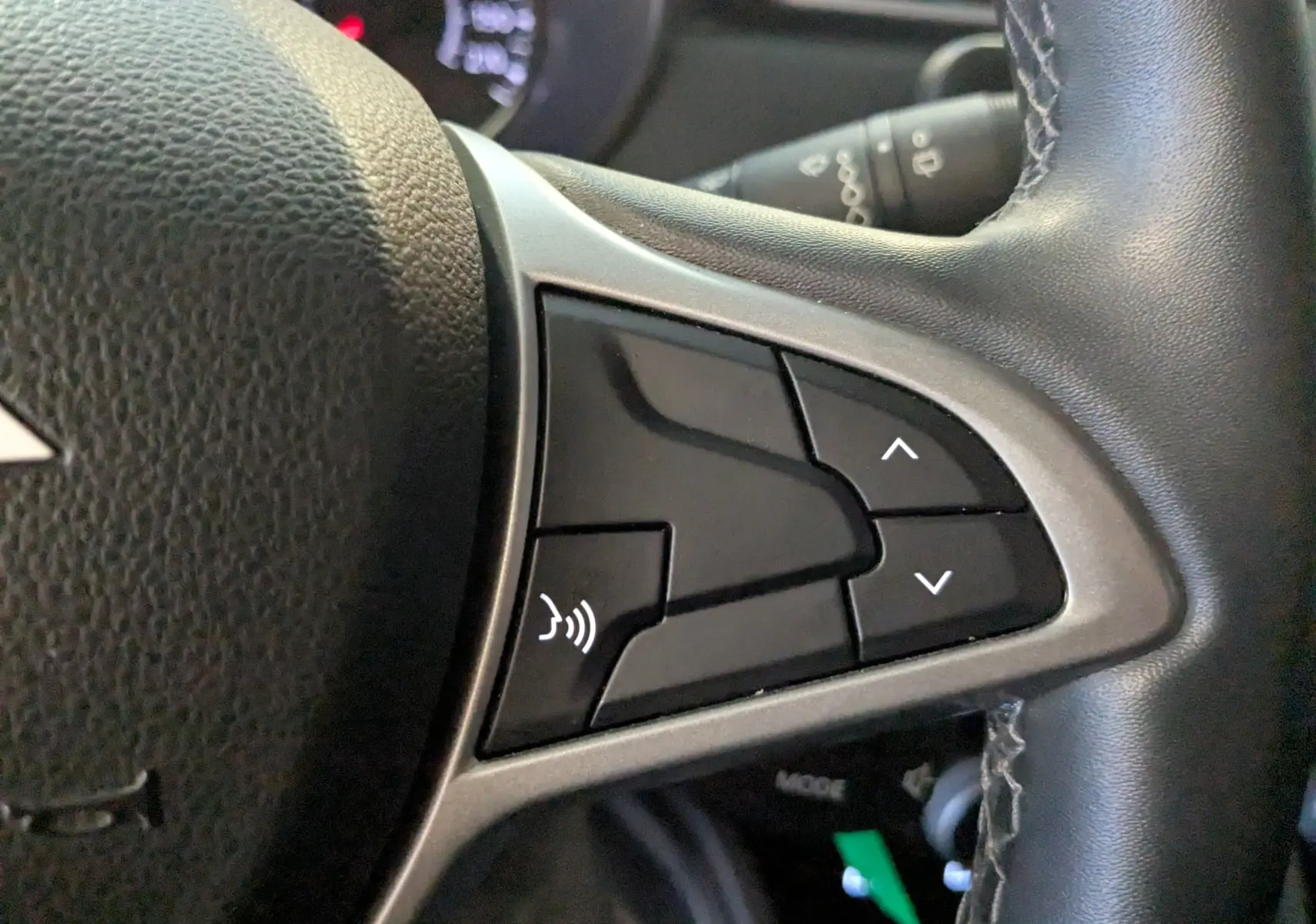 Gros plan sur les commandes vocales et de navigation au volant en cuir noir du Dacia Duster gris 2023.