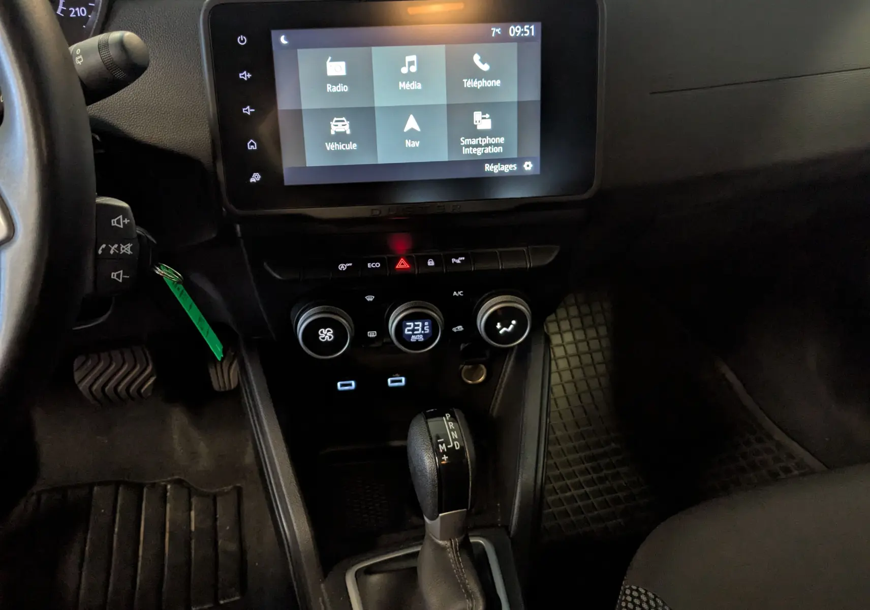 Vue intérieure du tableau de bord du Dacia Duster 2023 gris, avec écran tactile et levier de vitesse automatique visible.