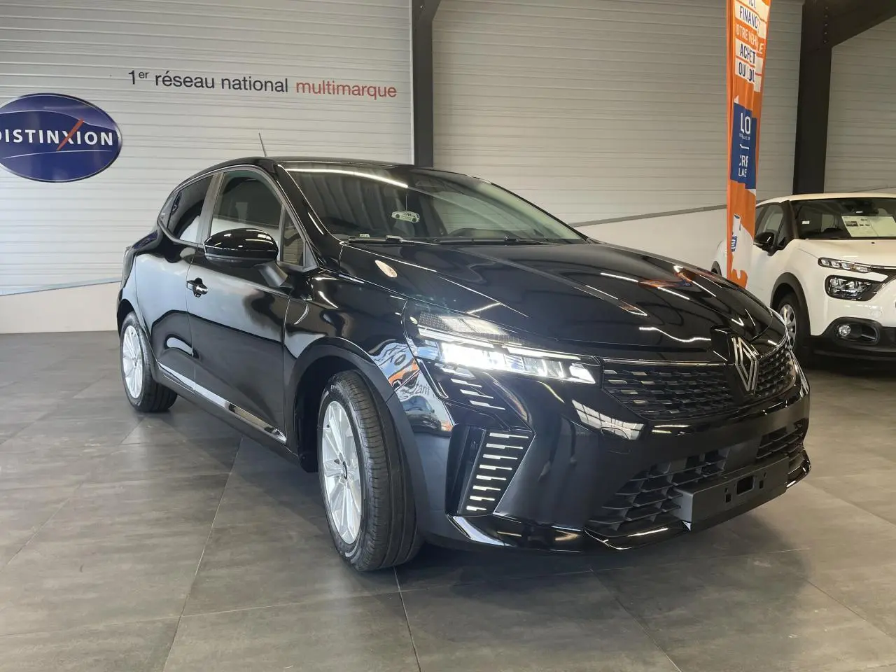 Renault Clio 2025 noir étoilé en 3/4 avant droit, avec jantes alu et feux LED allumés en showroom.
