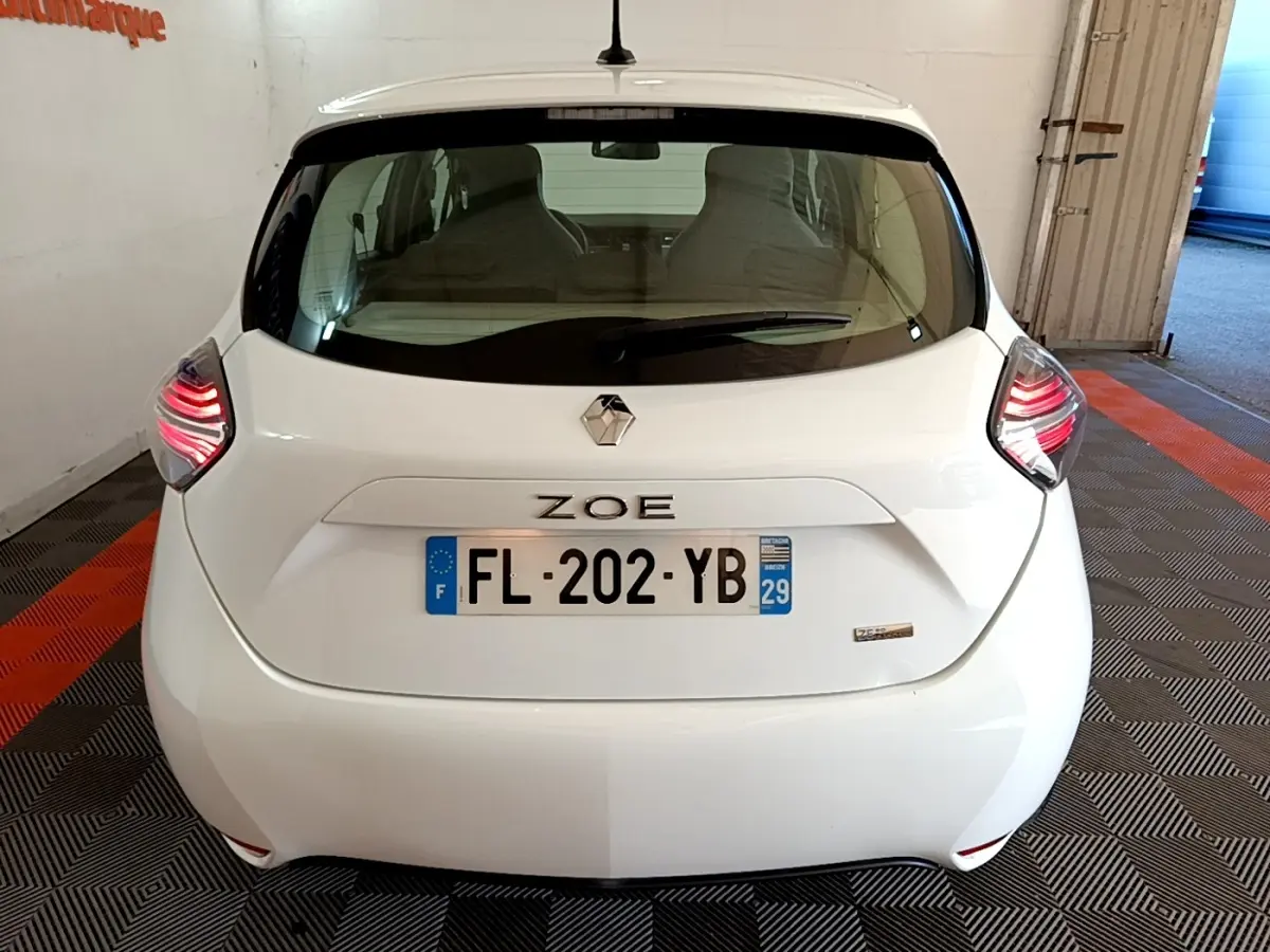 Vue arrière d'une Renault ZOE blanche avec feux LED allumés, plaque d'immatriculation française visible.