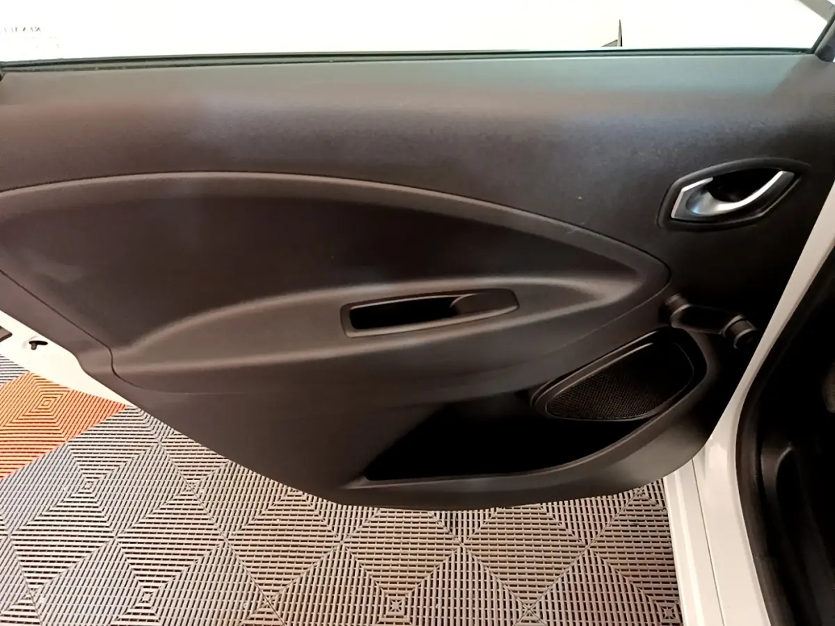 Vue rapprochée de la porte intérieure côté droit noire de la Renault ZOE blanche, avec poignée et haut-parleur intégrés.