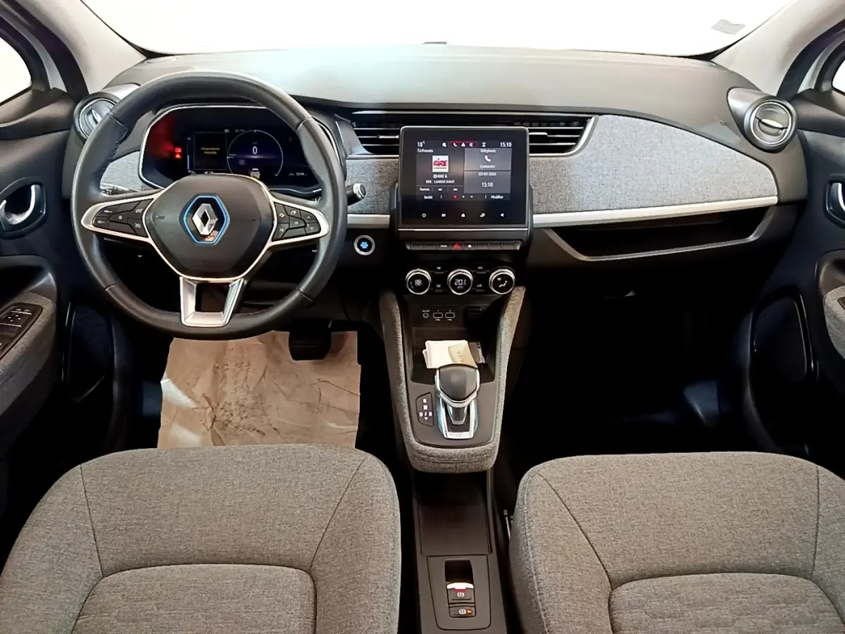 Vue intérieure avant de la Renault ZOE Zen R110 blanche, tableau de bord avec écran tactile central et volant multifonctions.