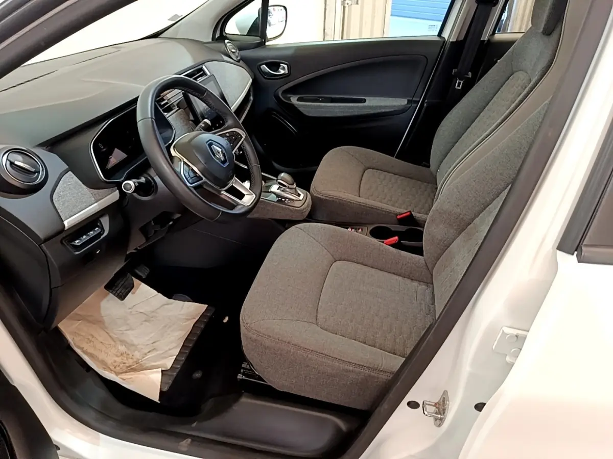 Vue intérieure côté conducteur de la Renault ZOE blanche 2019, sièges gris et tableau de bord avec écran tactile.