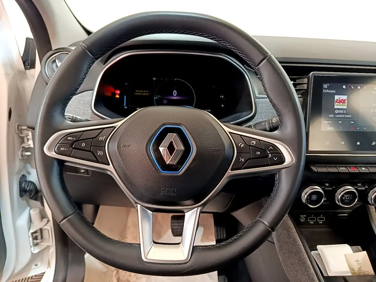 Vue intérieure centrée sur le volant noir de la Renault ZOE blanche avec tableau de bord digital et écran tactile.
