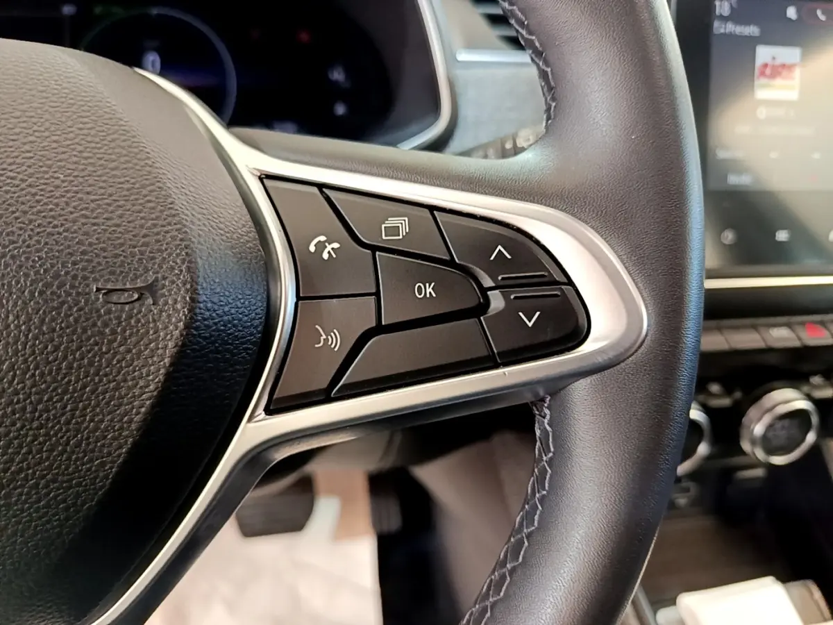 Gros plan sur les commandes multifonctions du volant en cuir noir de la Renault ZOE blanche, avec écran tactile en arrière-plan.