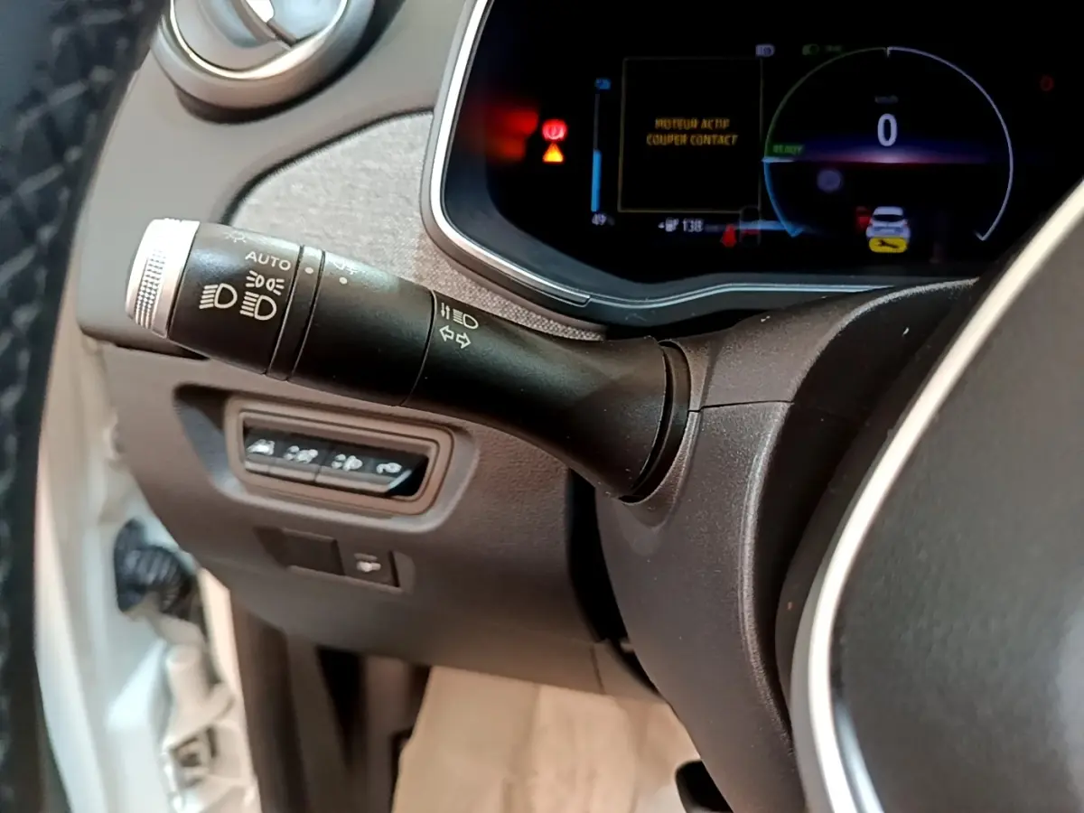 Gros plan sur la commande des phares et clignotants à gauche du volant dans le tableau de bord numérique d’une Renault ZOE blanche.