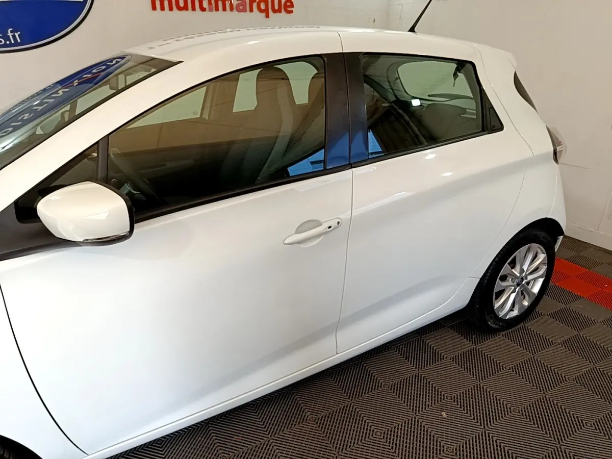 Vue latérale côté gauche d'une Renault ZOE blanche 2019 en intérieur, avec rétroviseur et poignées de porte visibles.