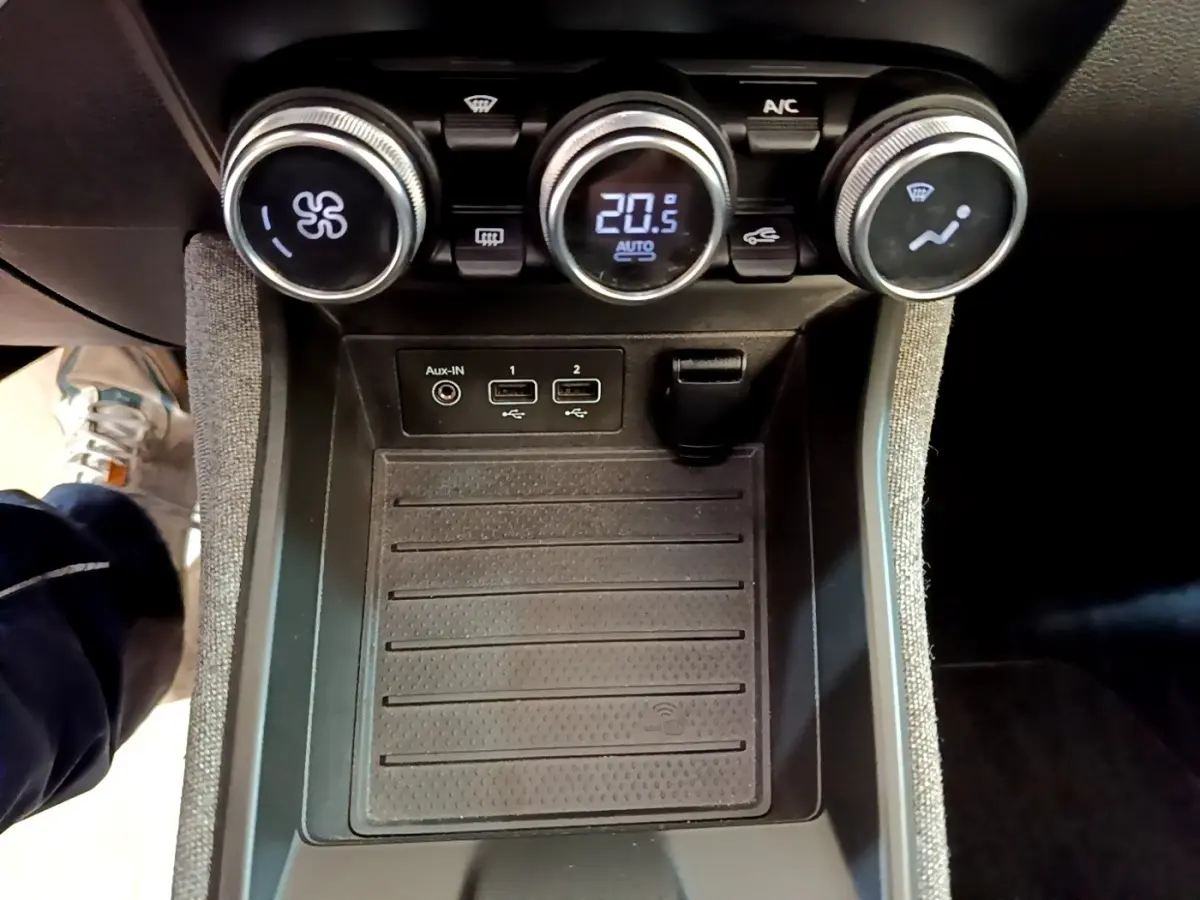 Vue rapprochée du tableau de bord central de la Renault ZOE Zen R110 blanc, montrant les commandes de climatisation et la zone de recharge par induction.